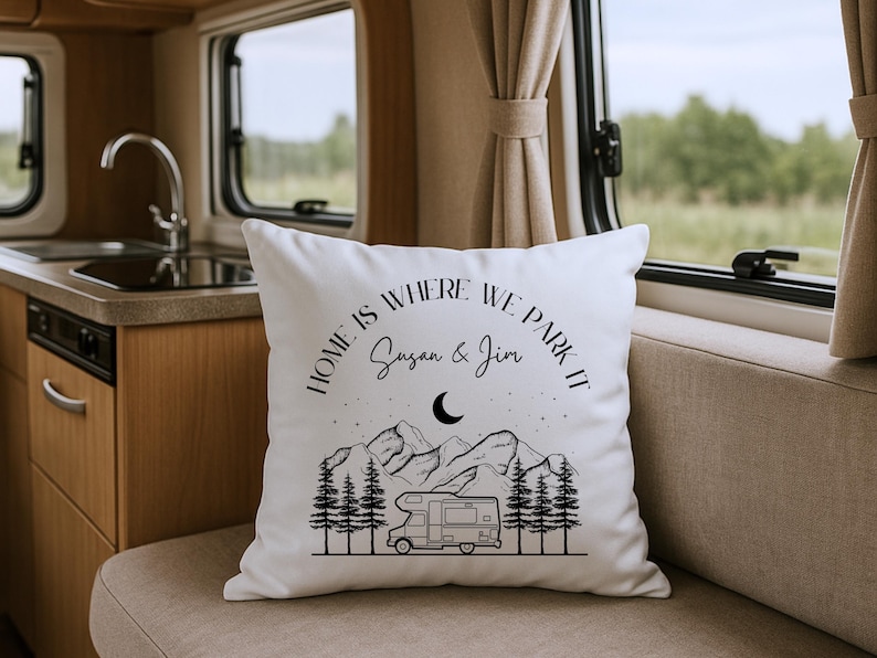 May include: A white square throw pillow featuring a black line art graphic of a camper van, pine trees, mountains, stars, and a crescent moon. The text reads "HOME IS WHERE WE PARK IT" above the names "Susan & Jim" in a script font.