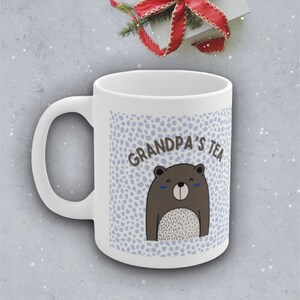 May include: White ceramic mug with a blue and white polka dot pattern. The mug has a brown bear with a white belly and the text "Grandpa's Tea" on it.
