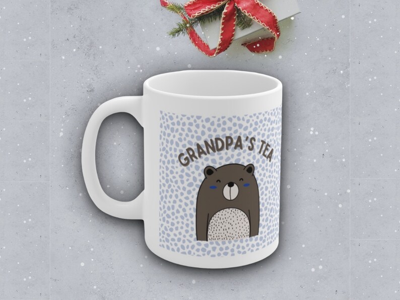 May include: White ceramic mug with a blue and white polka dot pattern. The mug has a brown bear with a white belly and the text "Grandpa's Tea" on it.
