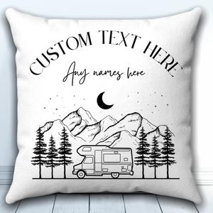May include: A white square throw pillow featuring a black line art illustration of a camper van parked in front of a forest and mountains under a crescent moon and stars. The text CUSTOM TEXT HERE and Any names here are printed above.