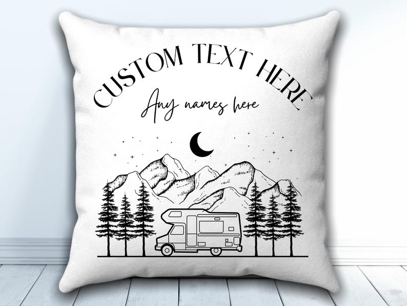 May include: A white square throw pillow featuring a black line art illustration of a camper van parked in front of a forest and mountains under a crescent moon and stars. The text CUSTOM TEXT HERE and Any names here are printed above.