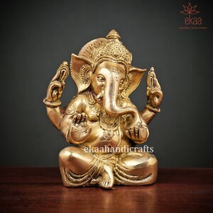 May include: A gold-colored brass statue of Ganesha, the Hindu god of wisdom and prosperity, sitting in a meditative pose with his trunk raised. The statue is intricately detailed with ornate jewelry and a crown.