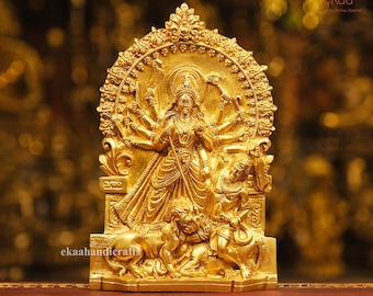 May include: A gold-colored metal statue of a Hindu goddess with multiple arms, sitting on a throne with two lions at her feet. The statue is intricately detailed and has a traditional design.
