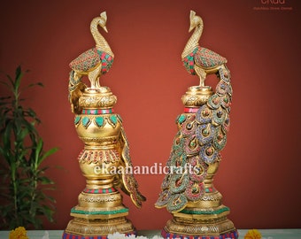 May include: A pair of gold peacock statues with colorful gemstone accents. The peacocks are standing on ornate bases with intricate details. The statues are a traditional Indian design and would make a beautiful addition to any home.