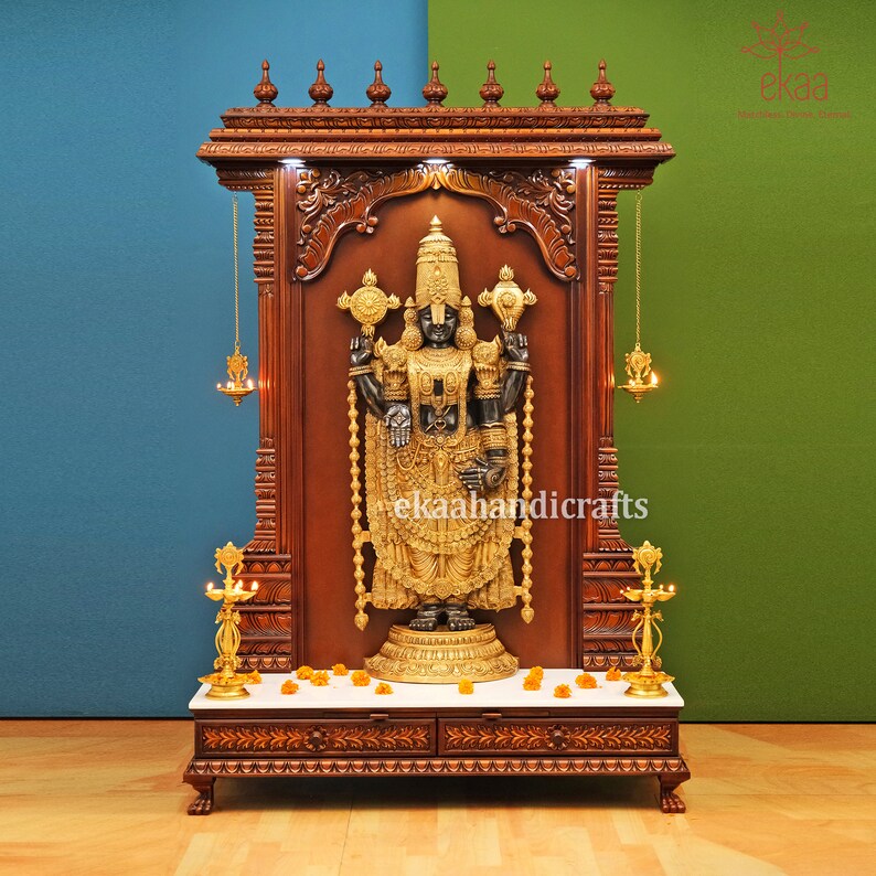May include: A wooden shrine with intricate carvings, featuring a black and gold statue of a deity. The shrine has a white marble platform and two decorative lamps on either side.