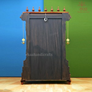 May include: A dark wood temple-style cabinet with intricate carvings and gold accents. The cabinet has two doors and a shelf inside. The cabinet is decorated with two brass oil lamps hanging from chains.
