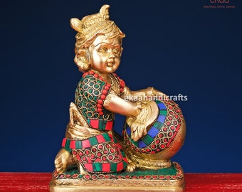 May include: A gold-coloured statue of a young boy playing a drum. The drum is decorated with colourful stones and the boy is wearing a green and red patterned outfit.
