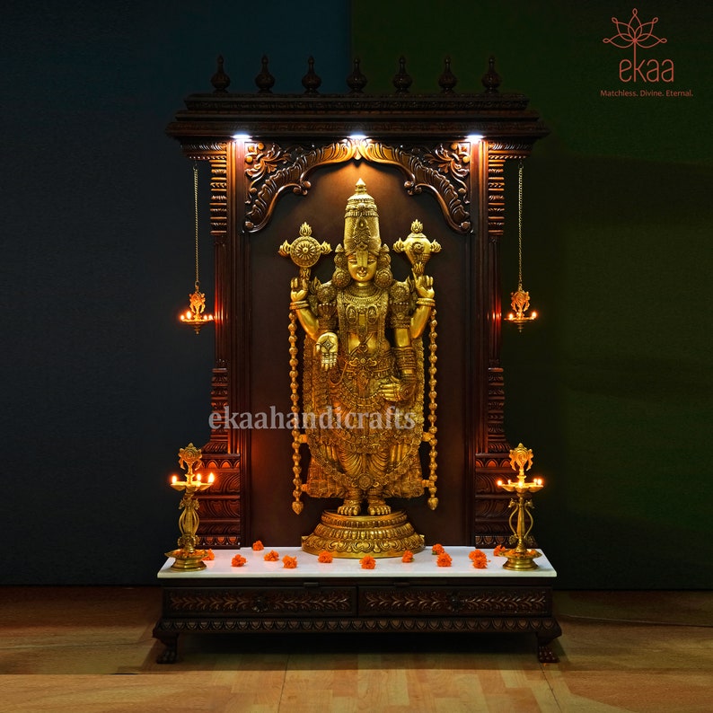 May include: A dark wood temple with intricate carvings and gold accents. A golden statue of a deity stands in the center, with a white marble platform below. The temple has two small brass lamps on either side of the statue.
