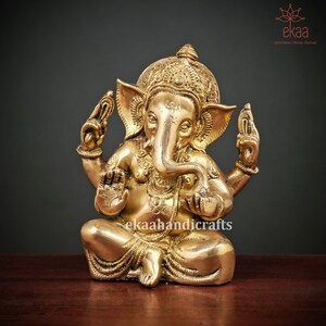 May include: A gold-colored brass statue of the Hindu deity Ganesha, sitting with his trunk raised and hands in a gesture of blessing. The statue is intricately detailed with decorative patterns and is a traditional symbol of good luck and prosperity.