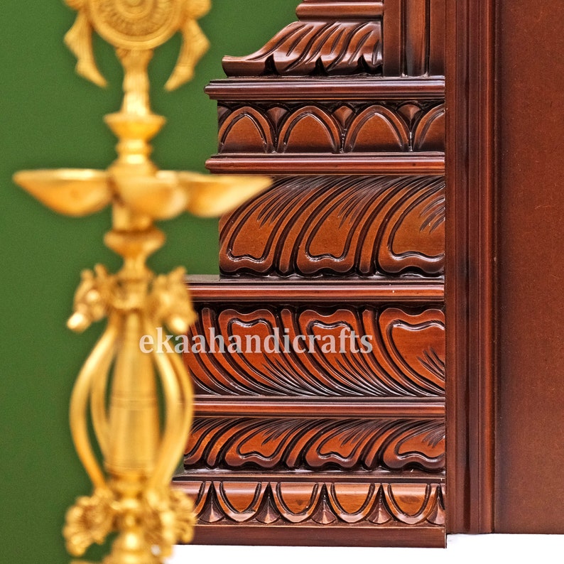 May include: Close-up of a richly carved wooden frame with intricate details. The frame is a deep brown color and features a series of decorative patterns, including waves and floral motifs. The frame is likely part of a larger piece of furniture, such as a door or a cabinet.