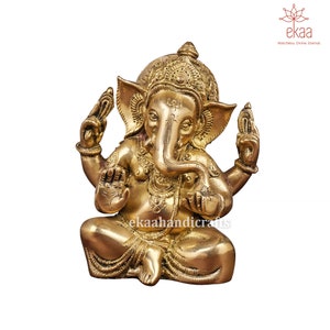 May include: A gold-colored brass statue of Ganesha, the Hindu god of wisdom and prosperity, sitting in a meditative pose with his trunk raised and his hands in a gesture of blessing. The statue is intricately detailed with decorative patterns and a crown on Ganesha's head.