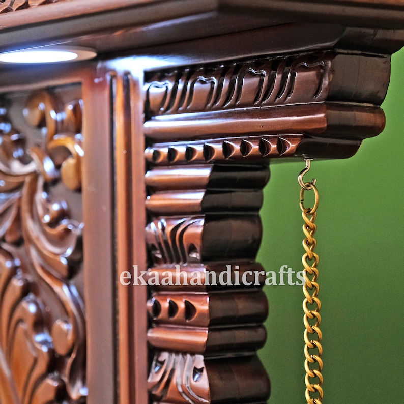 May include: Close-up of a dark brown wooden shelf with intricate carvings. A gold chain hangs from a hook on the shelf. The text "ekaahandicrafts" is visible on the shelf.