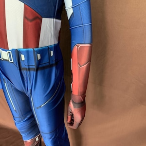 May include: A blue and red spandex costume with a white star on the chest. The costume has a belt with a silver buckle and a red and blue arm covering.