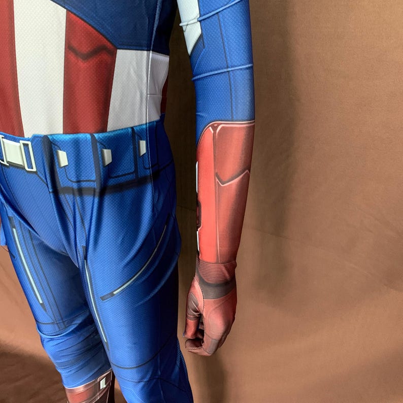May include: A blue and red spandex costume with a white star on the chest. The costume has a belt with a silver buckle and a red and blue arm covering.