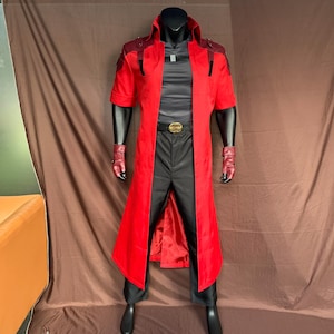 Op de afbeelding: Een rood cosplaykostuum op een mannequin. Het kostuum omvat een lange rode jas met korte mouwen, een zwarte broek, een zwart shirt en rode polsmanchetten. Een gouden gesp en zwarte laarzen maken de outfit compleet.