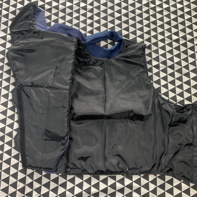 Pu&ograve; includere: Un giubbotto trapuntato nero con fodera blu navy. Il giubbotto ha una chiusura con cerniera e un colletto alto.
