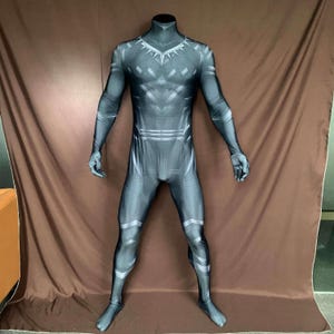May include: A black and grey full-body costume with a high collar and a detailed geometric pattern. The costume has silver accents and is designed to cover the entire body, including the hands and feet. The costume is displayed on a headless mannequin.