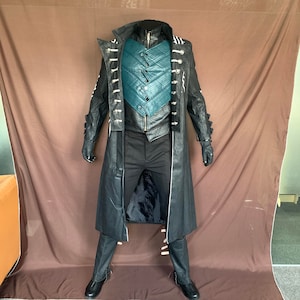 Może przedstawiać: Czarny skórzany płaszcz z turkusową kamizelką i srebrnymi guzikami. Płaszcz ma długi, płynny styl i jest noszony na czarnych spodniach.