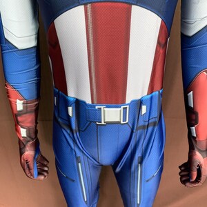 May include: A blue and red superhero costume with a white star on the chest. The costume has a belt with a silver buckle and a zip down the front.