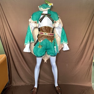 May include: A green and white costume with a flower on the hat. The costume includes a green and white cape, a brown leather belt with a gold buckle, and green shorts. The costume is worn by a person with white tights and brown shoes.