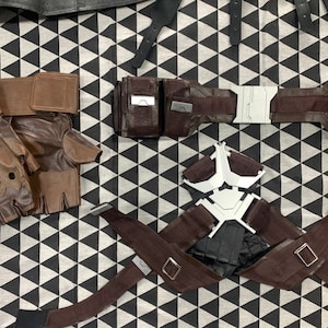 Pu&ograve; includere: Un set di accessori in pelle marrone per cosplay o costume. Il set include un paio di guanti senza dita, una cintura con una fibbia argentata e un'imbracatura con una fibbia argentata a forma di stella.