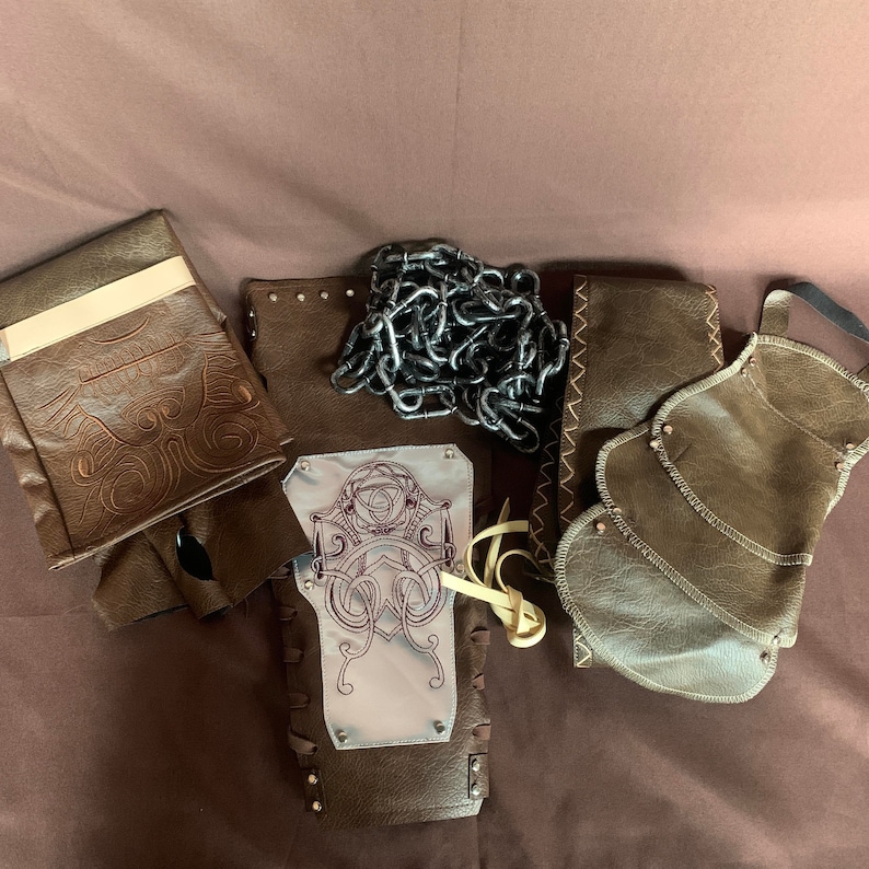 Puede incluir: Un conjunto de piezas de armadura de cuero marr&oacute;n con dise&ntilde;os intrincados. La armadura incluye una pieza de pecho, hombreras y un cintur&oacute;n. La pieza de pecho tiene una placa de metal plateado con un dise&ntilde;o decorativo. Las hombreras tienen un dise&ntilde;o de malla de cadena. El cintur&oacute;n tiene una hebilla con un dise&ntilde;o decorativo.