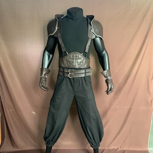 Könnte beinhalten: Ein braunes Lederkostüm mit einem schwarzen Rollkragenpullover, einem Bruststück, Schulterpolstern und einer schwarzen Hose. Das Kostüm wird von einer Schaufensterpuppe getragen.