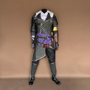 Può includere: Un costume cosplay completo su un manichino. L'outfit presenta una giacca nera e grigia con dettagli bianchi, una fascia viola e pantaloni neri. La giacca ha un colletto di pelliccia bianca e dettagli dorati. Gli stivali sono neri con dettagli bianchi.