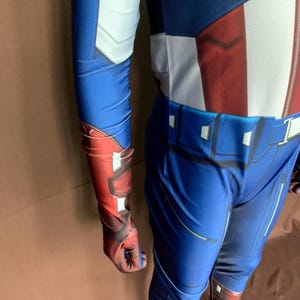 May include: A blue and red spandex costume with a white star on the chest. The costume has a belt and a zip on the front. The costume is designed to look like a superhero.