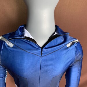 May include: Close-up of the zipper and neckline of a blue and white superhero costume. The costume has a black zipper and a white lining.