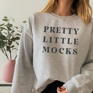 May include: A gray sweatshirt with the text "PRETTY LITTLE MOCKS" printed in black.