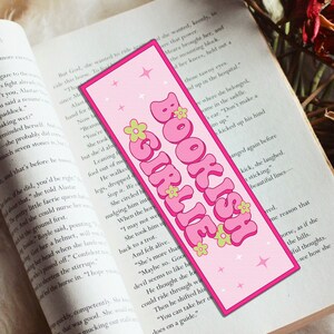 May include: Pink and green bookmark with the text "BOOKISH GIRLIE" in a retro font. The bookmark has a pink background with white stars and green flowers.