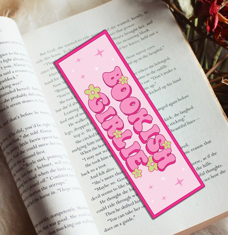 May include: Pink and green bookmark with the text "BOOKISH GIRLIE" in a retro font. The bookmark has a pink background with white stars and green flowers.