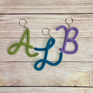May include: Three crocheted letter keychains in the shape of the letters A, B, and L. The A is green, the B is purple, and the L is blue.
