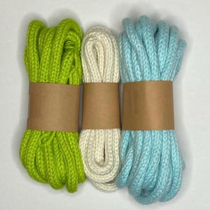 May include: Three spools of cotton cord, one green, one white, and one light blue. Each spool is wrapped in brown paper.