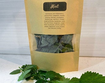 Könnte beinhalten: Ein Kraftpapierbeutel mit getrockneten Minzblättern mit einem transparenten Fenster und einem Zweig frischer Minze. Der Beutel trägt den Text "Mint" und eine Liste von Vorteilen. Die frische Minze hat grüne Blätter und Stängel.