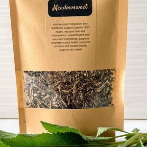 May include: A kraft paper bag of dried meadowsweet leaves with a clear window, a pile of dried leaves, and fresh green leaves. The bag has the text "Meadowsweet" and other text describing the product's benefits.