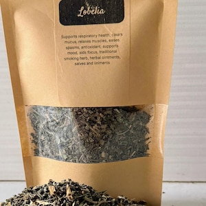 May include: A kraft paper bag of dried Lobelia leaves with a clear window, and a pile of loose leaves in front. The bag has text that reads "Dried Leaves" and "Lobelia". The text also mentions the product is organic and hand-picked.
