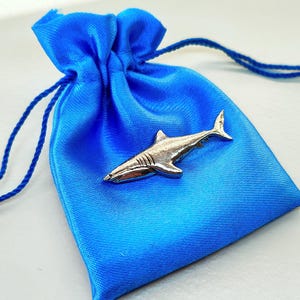 May include: A small silver shark figurine in a blue satin drawstring bag.