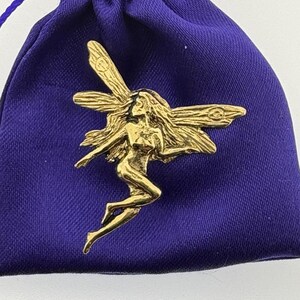 May include: A gold-coloured fairy figurine with wings outstretched, sitting on a purple velvet pouch.