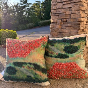 May include: Two square throw pillows featuring a printed landscape scene of green hills and trees. The left pillow has a textured red floral pattern on the upper half, while the right pillow displays a similar red floral pattern on the lower half.