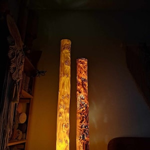 May include: Two tall wooden lamps with a natural wood finish. The lamps are lit and casting a warm glow. The lamps are on a wooden table.