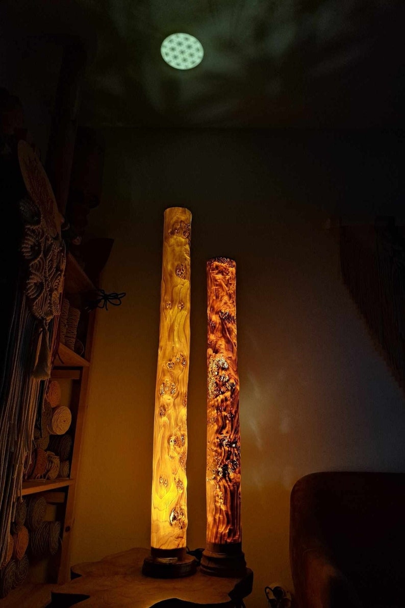 May include: Two tall wooden lamps with a natural wood finish. The lamps are lit and casting a warm glow. The lamps are on a wooden table.