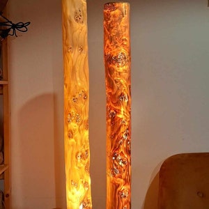 May include: Two wooden lamps with warm, glowing light inside. The lamps are made from natural wood with a unique grain pattern. They are sitting on a wooden table.
