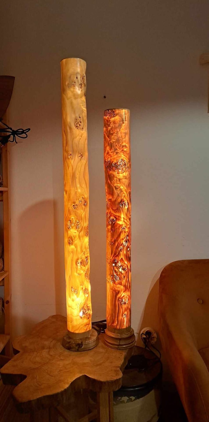 May include: Two wooden lamps with warm, glowing light inside. The lamps are made from natural wood with a unique grain pattern. They are sitting on a wooden table.