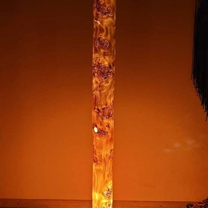 May include: A tall, cylindrical floor lamp made from a natural wood log with a warm, orange glow emanating from the light source inside. The lamp has a simple, wooden base.