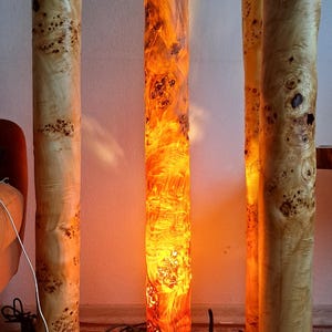 May include: Three wooden floor lamps with a natural wood finish and a warm, orange glow. The lamps are made from a single piece of wood and have a unique, organic shape.