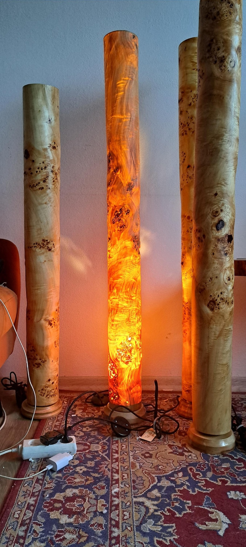 May include: Three wooden floor lamps with a natural wood finish and a warm, orange glow. The lamps are made from a single piece of wood and have a unique, organic shape.