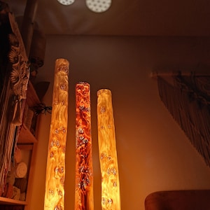 May include: Three wooden lamps with a warm, orange glow. The lamps are made from natural wood with a unique grain pattern. They are standing on a wooden base.