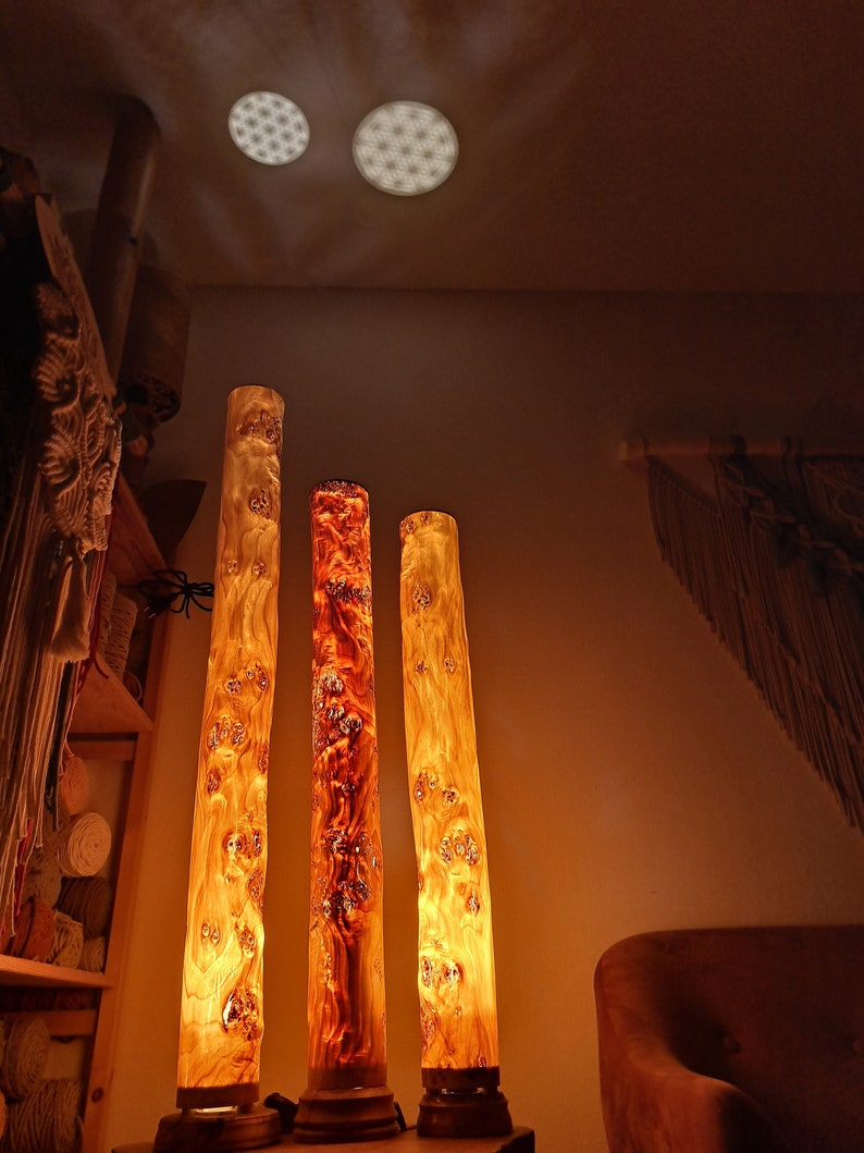 May include: Three wooden lamps with a warm, orange glow. The lamps are made from natural wood with a unique grain pattern. They are standing on a wooden base.
